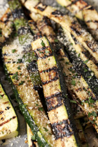 Side angle of grilled zucchini, garnished with grated Parmesan and parsley