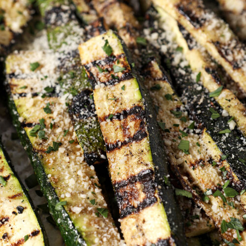 Side angle of grilled zucchini, garnished with grated Parmesan and parsley