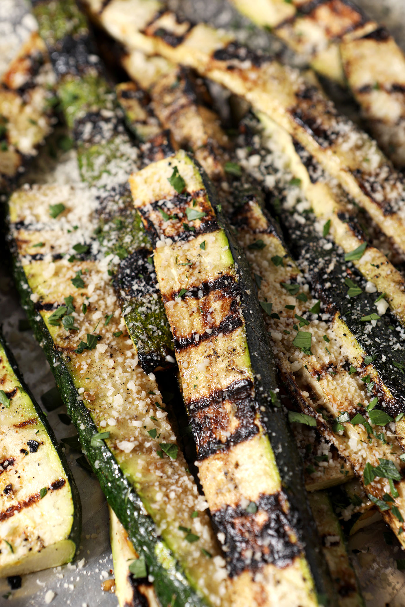 Side angle of grilled zucchini, garnished with grated Parmesan and parsley