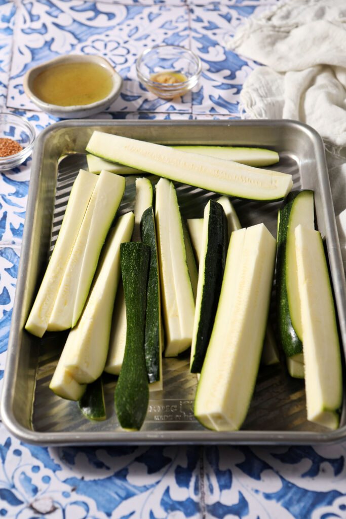 Sliced zucchini wedges on a sheet pan on a blue and white tiled surface