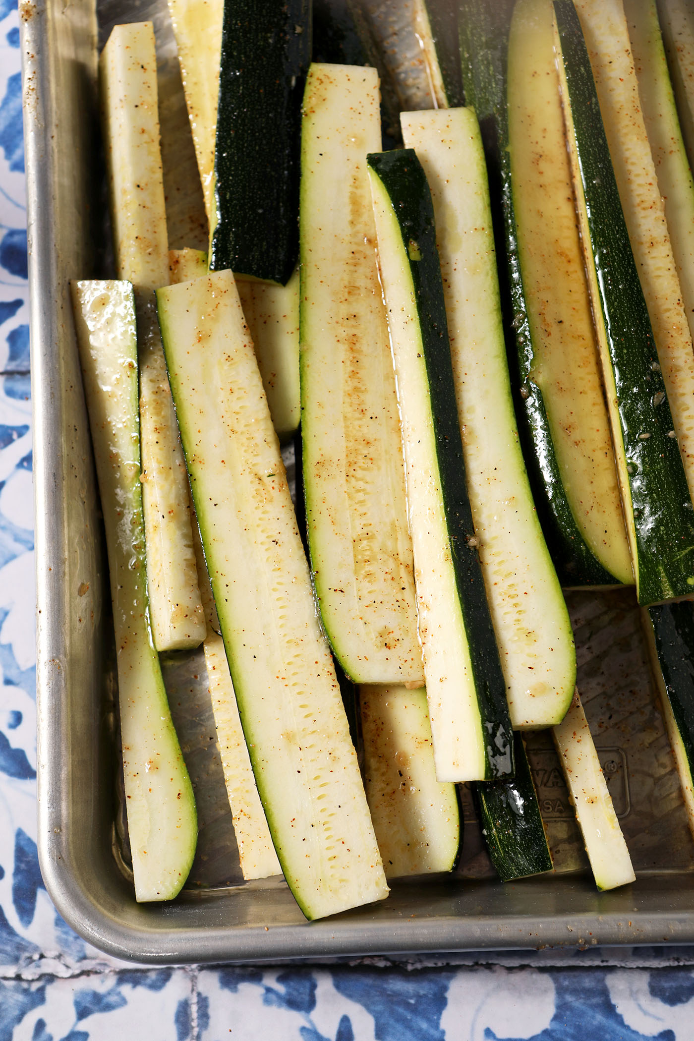 Seasoned zucchini wedges before grilling on a sheet pan