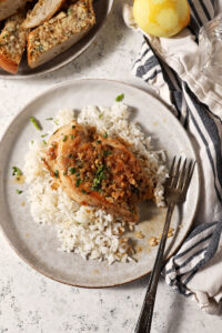 Lemon Garlic Chicken on a plate over rice with a plate of garlic bread and a lemon