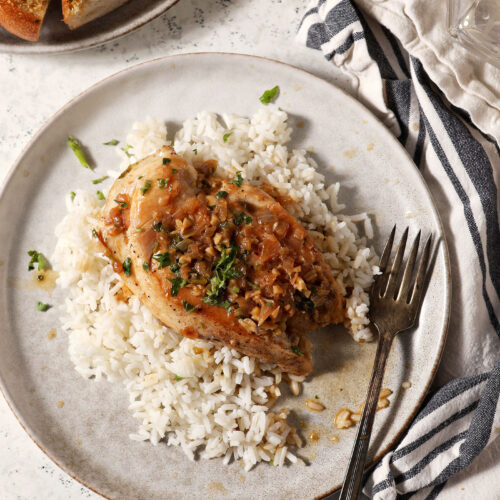 Lemon Garlic Chicken on a plate over rice with a plate of garlic bread and a lemon