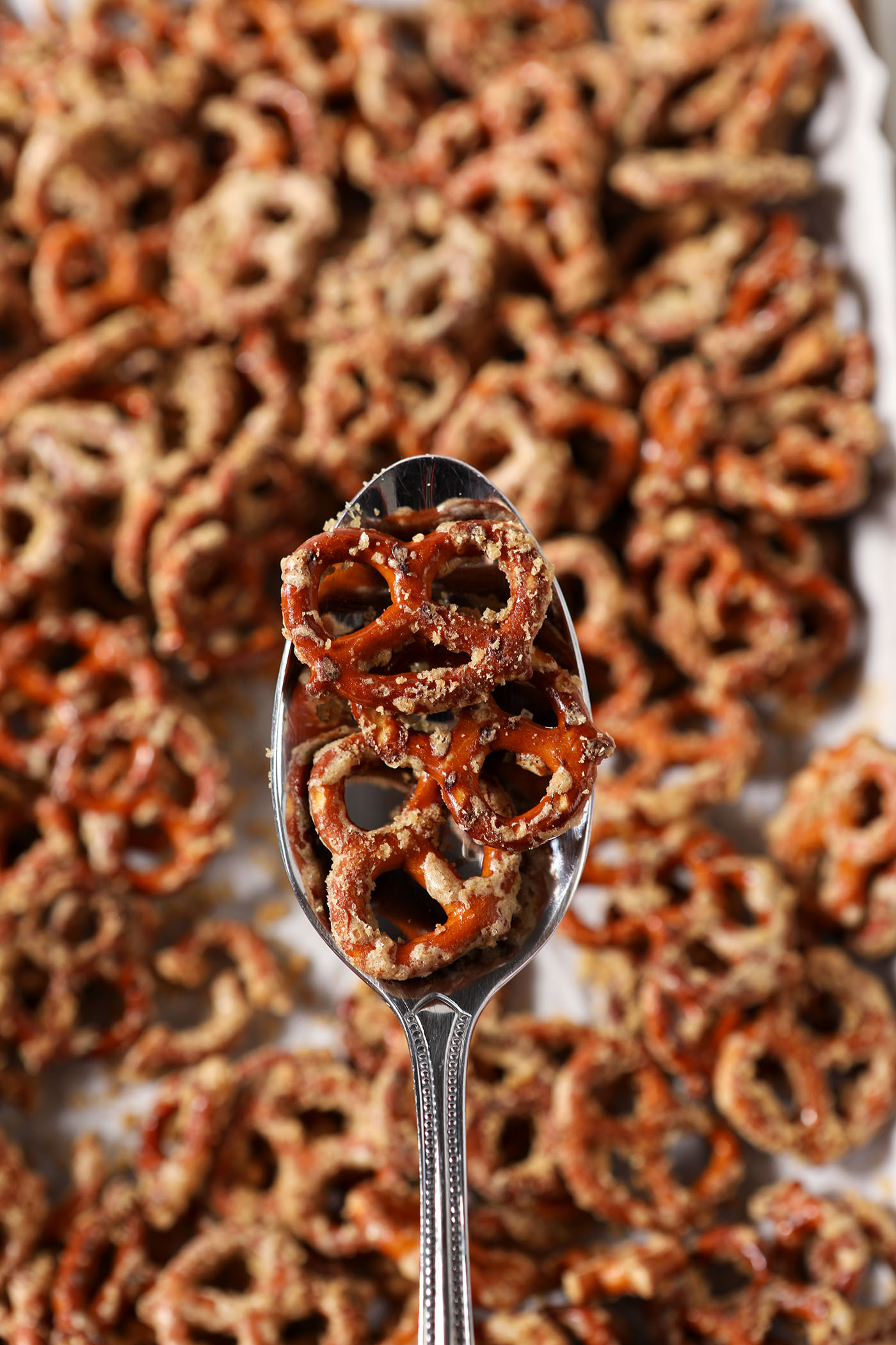 A spoon holds butter Toffee Pretzels above a sheet pan of more pretzels