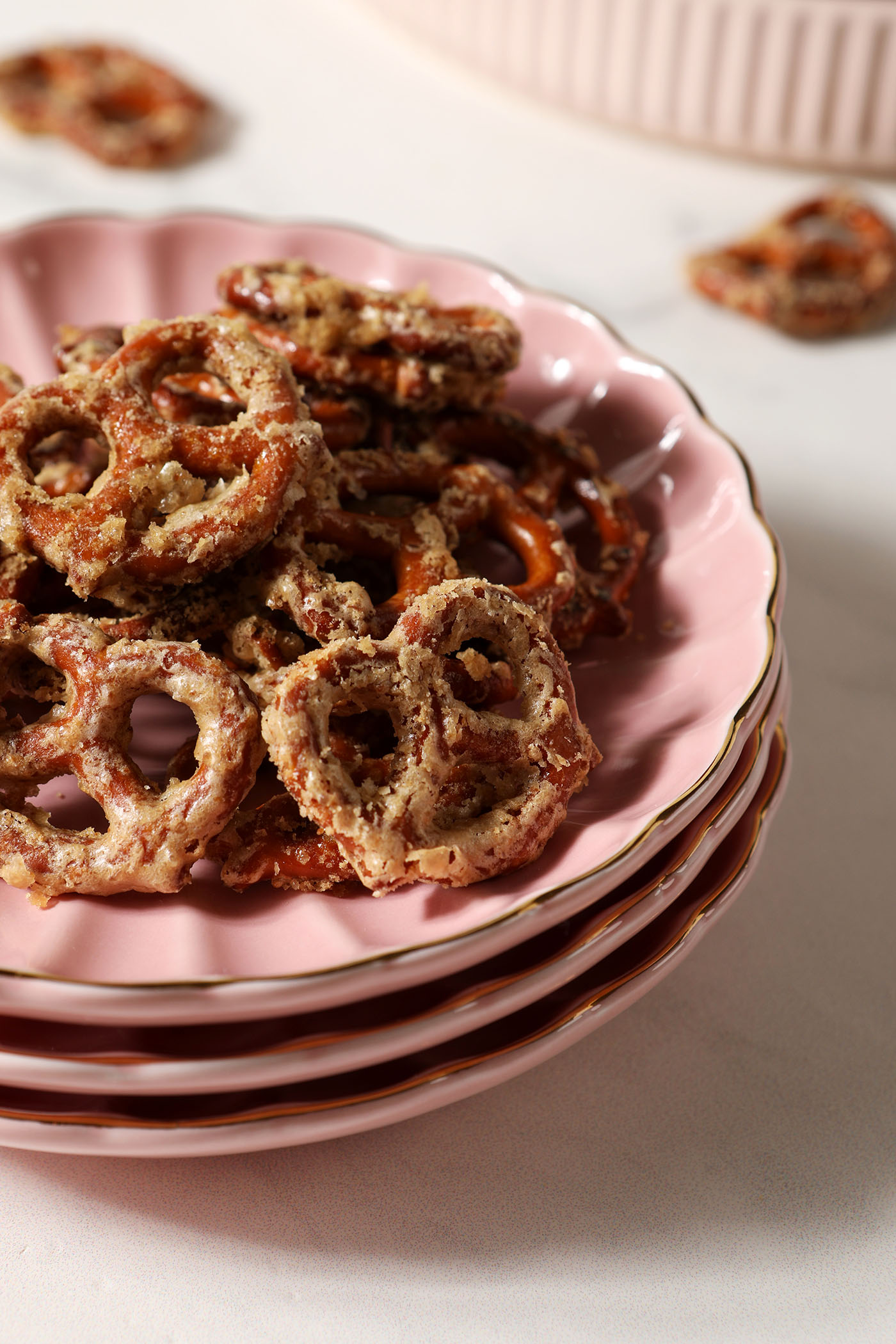 Side angle of butter Toffee Pretzels on a pink scalloped plate on a white stone surface