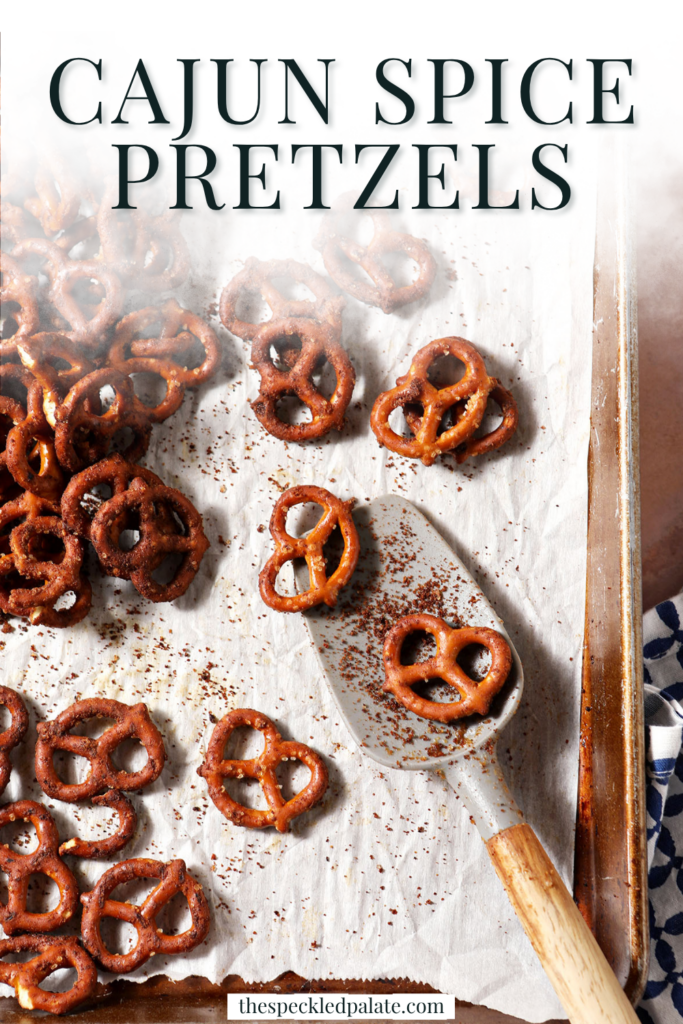 A spatula sits on a sheet pan of Cajun spice pretzels on a brick surface with a blue and white linen with the title, " Cajun Spice Pretzels" on top.