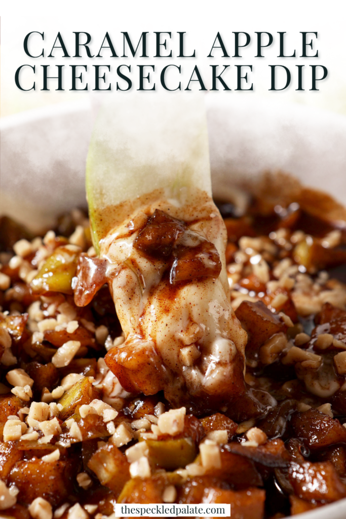 an Apple being pulled out of Caramel Apple Cheesecake Dip in a white serving dish with different dippers around it.