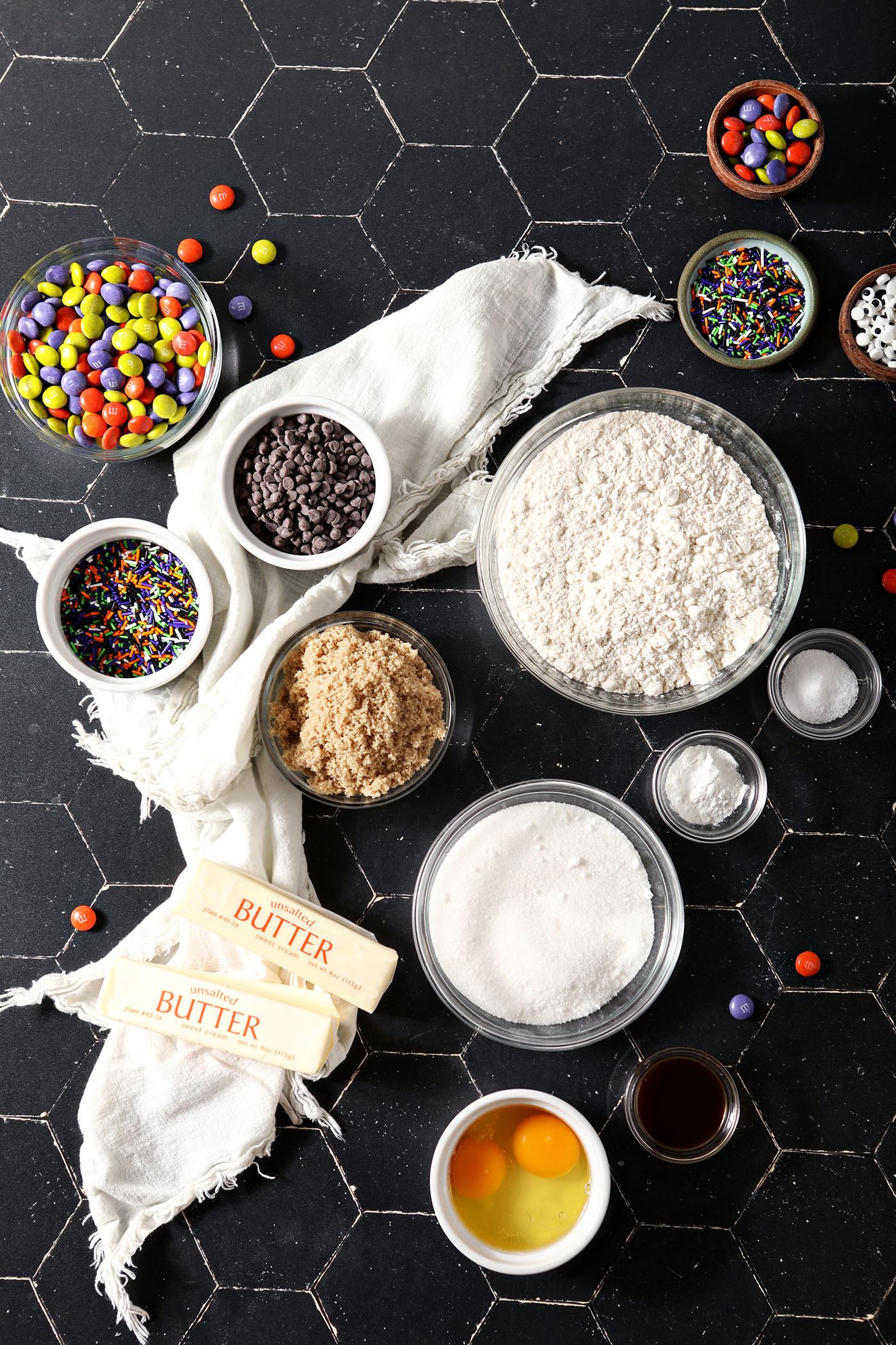 Bowls containing Halloween cookie ingredients on a black tiled surface