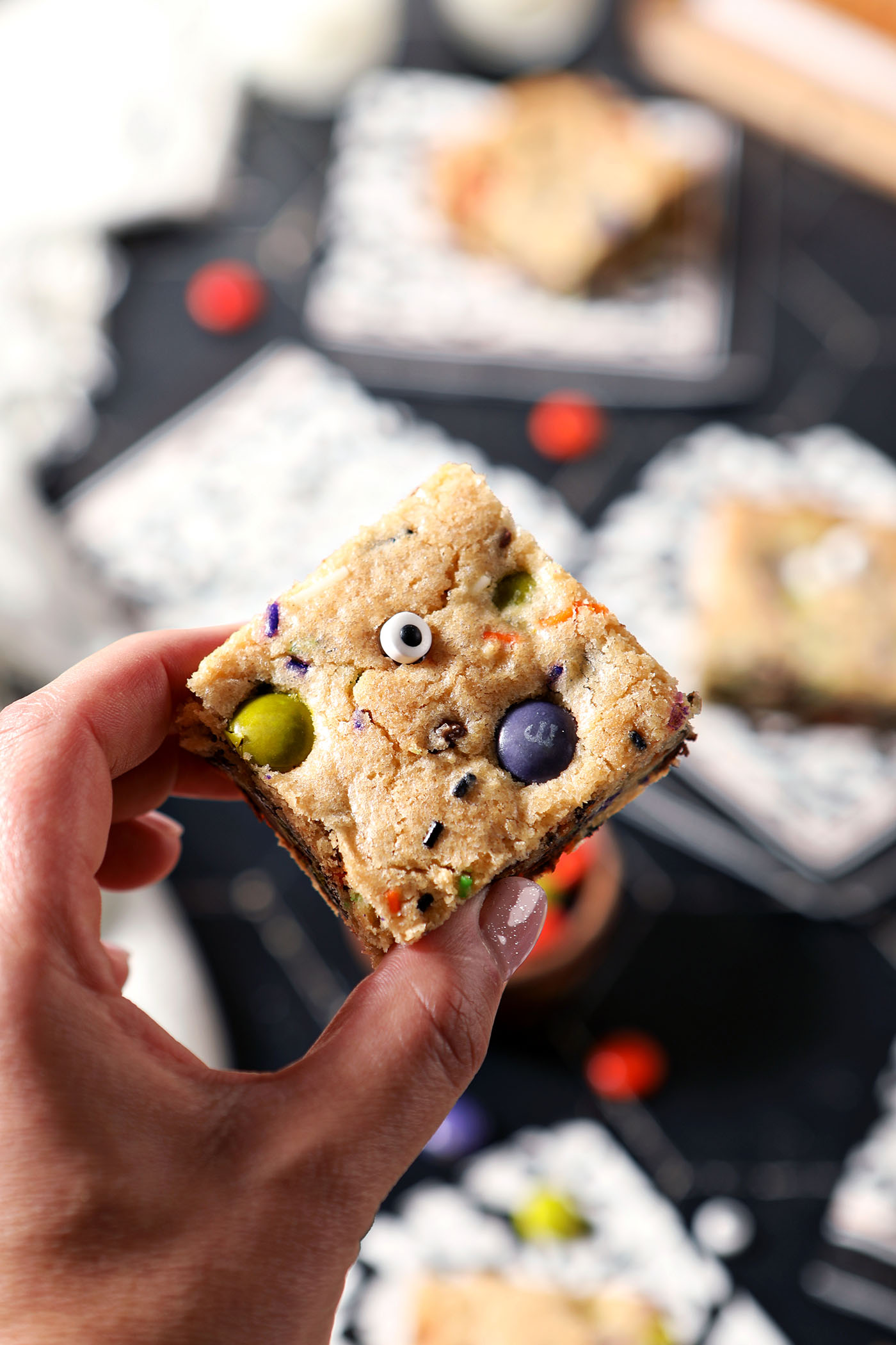 A hand holds a Halloween Cookie Bar above a black surface with more bars