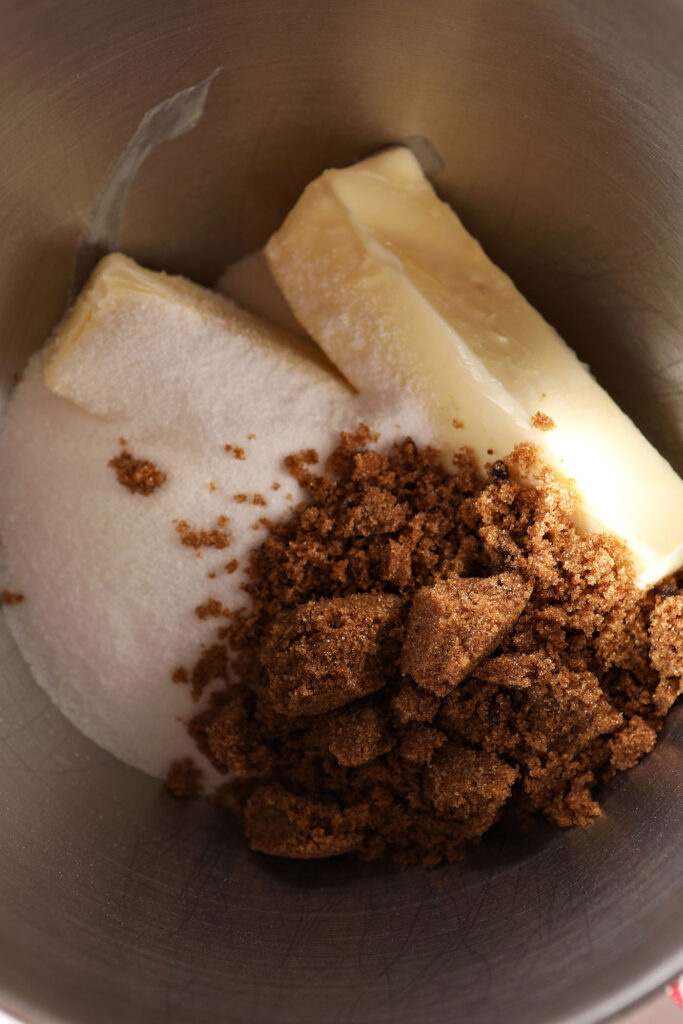 Sticks of butter in a metal bowl with brown and white sugars