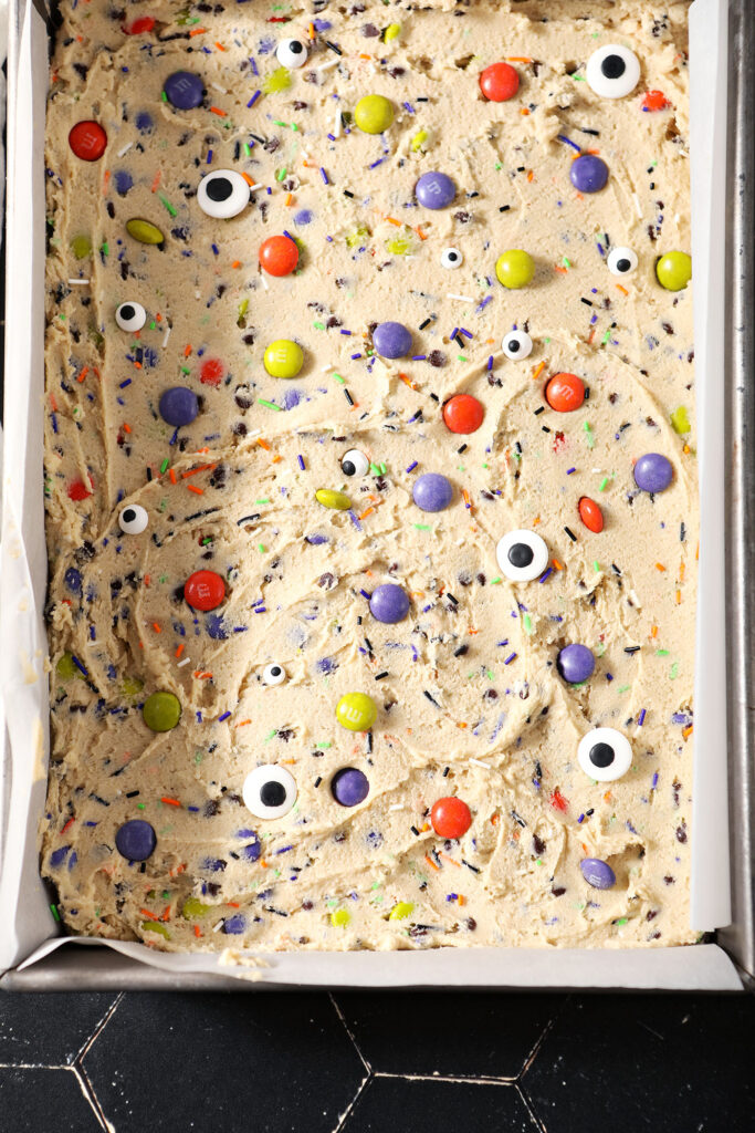 Halloween Cookie Bar cookie dough in a pan with decorations on top before baking