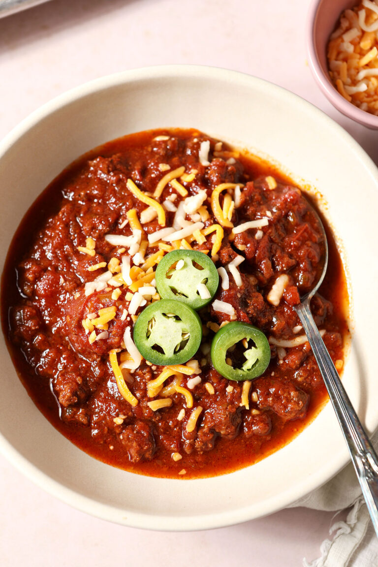 A bowl of spicy bison chili from above with a spoon, garnished with shredded cheese and jalape&ntilde;o
