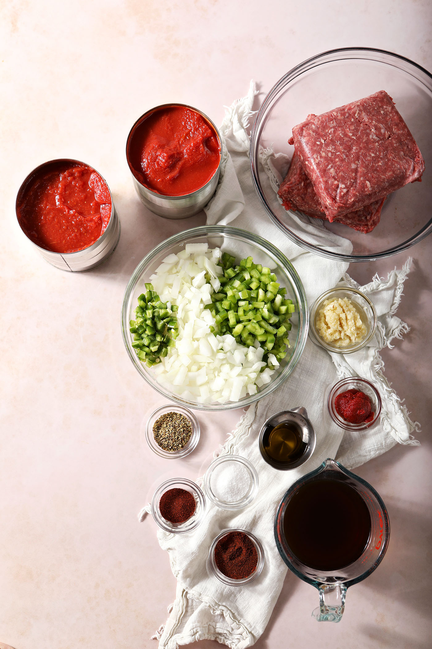 Ingredients to make bison chili in bowls on a tan surface