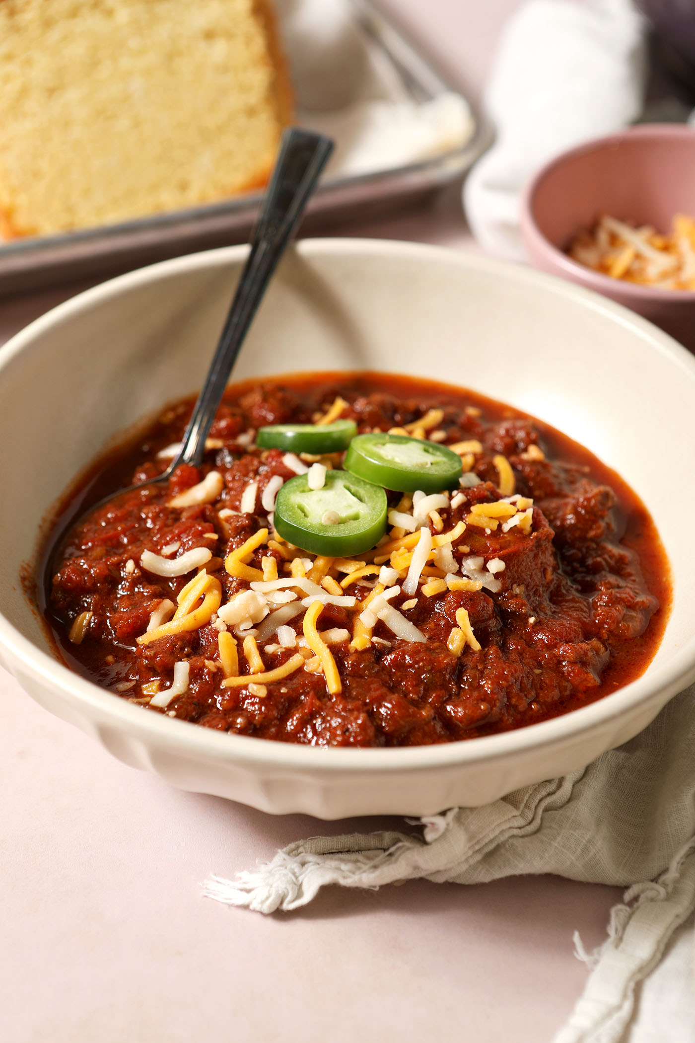 Side angle of a white bowl holding bison chili, garnished with shredded cheese and sliced jalapeño peppers