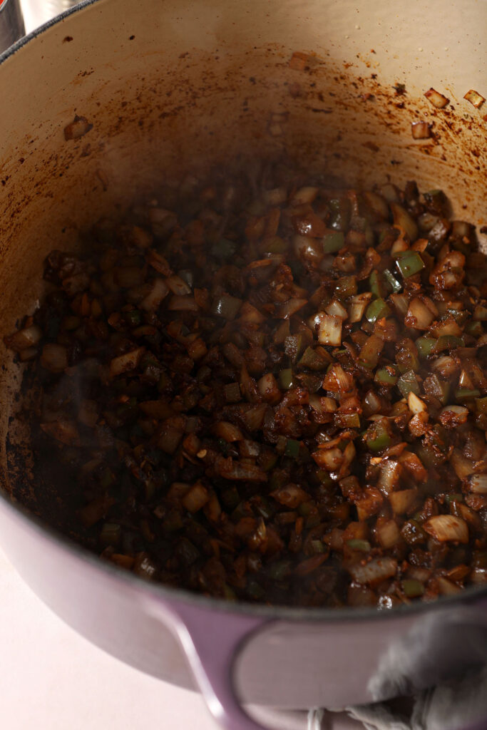 Cooked down vegetables and spices in a purple Dutch oven