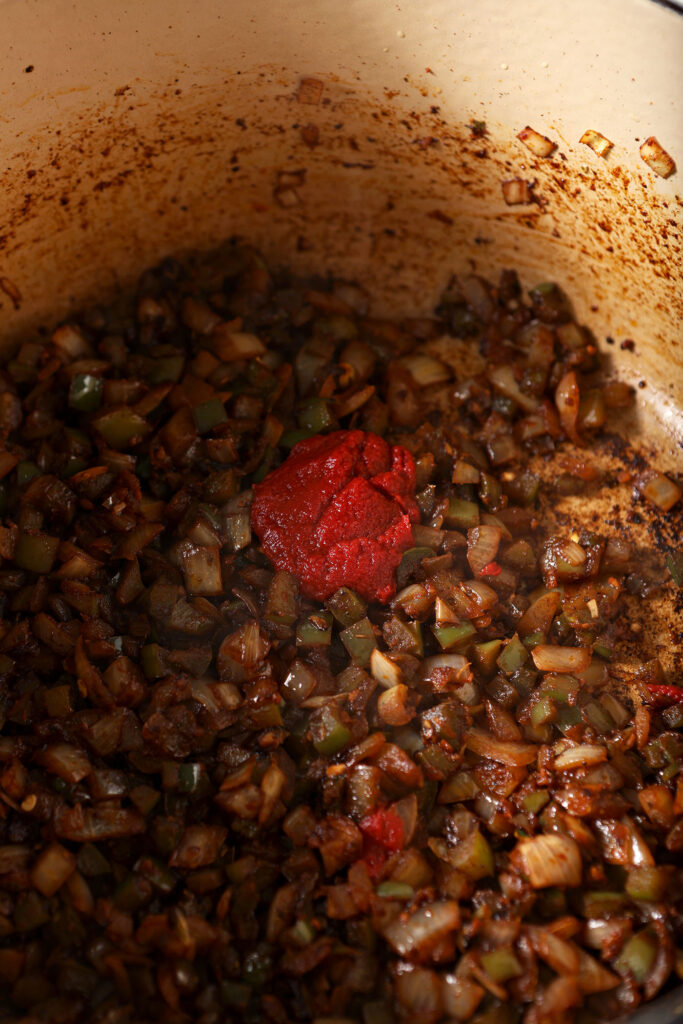 A large dollop of tomato paste on top of sautéed vegetables in a Dutch oven