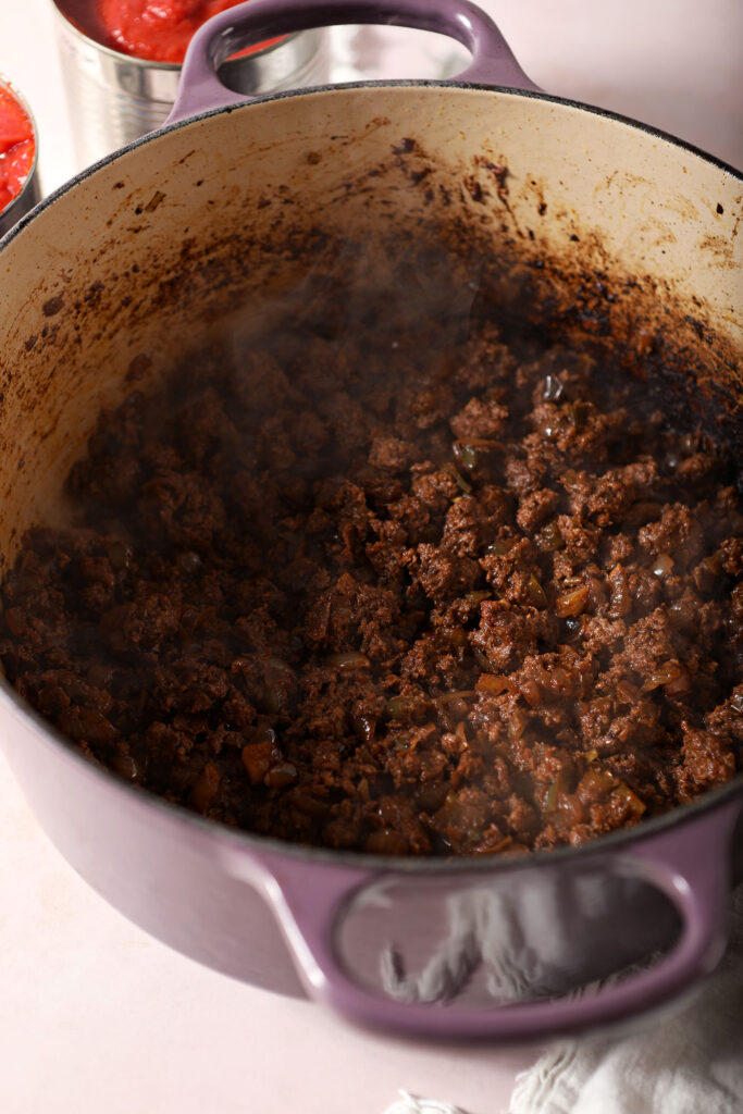 Cooked ground bison in a Dutch oven with other chili ingredients
