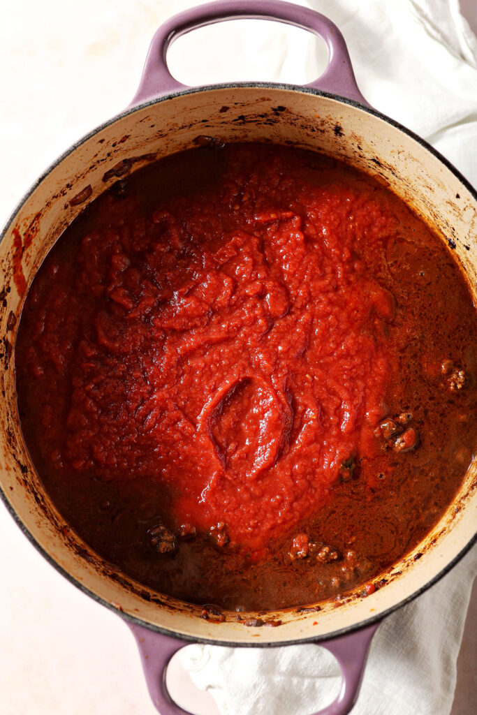 Crushed tomatoes and whole peeled tomatoes in a Dutch oven with ground bison and other ingredients to make chili