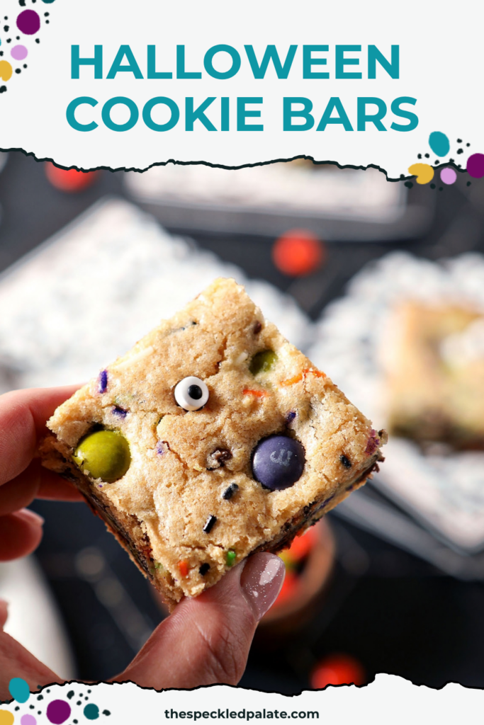 A hand holds a Halloween Cookie Bar above a black surface with more bars and Pinterest Title, "Halloween Cookie Bars" on top.